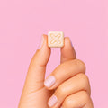Hand holding a small piece of gum with a 'X' symbol representing the FIIX logo on a pink background